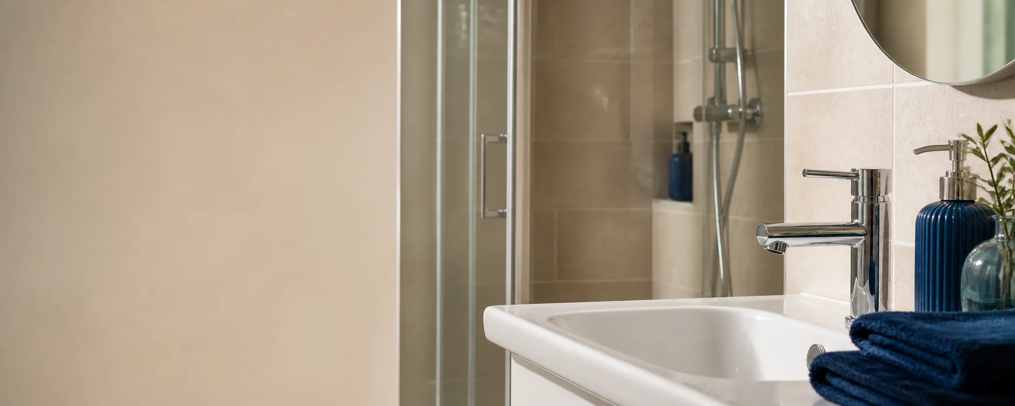 Illustrative bathroom with a chrome tap, white basin and glass shower screen.